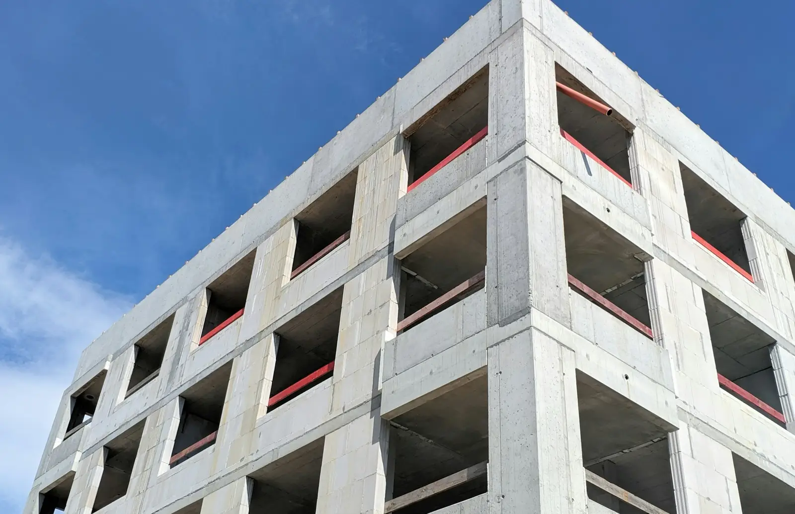 Mavi gökyüzü altında, pencere boşlukları açık beton karkas yapı